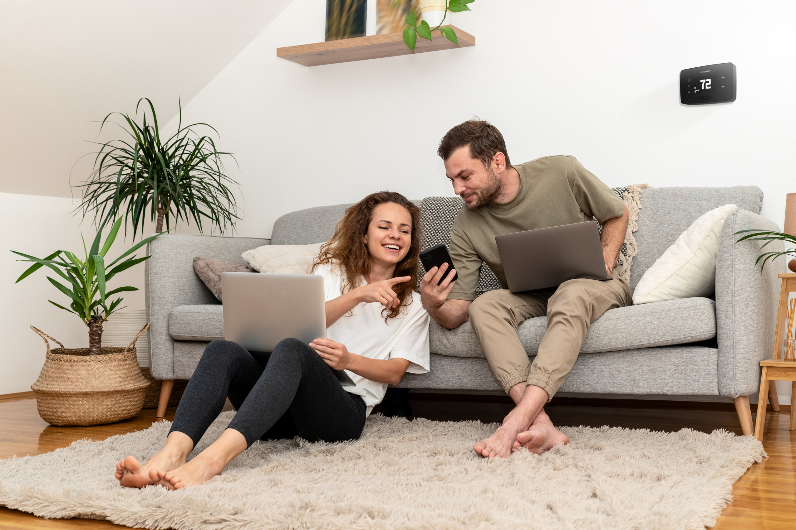 Man pointing on his phone to an energy management rebate with a Verdant VX4 smart thermostat installed in the room